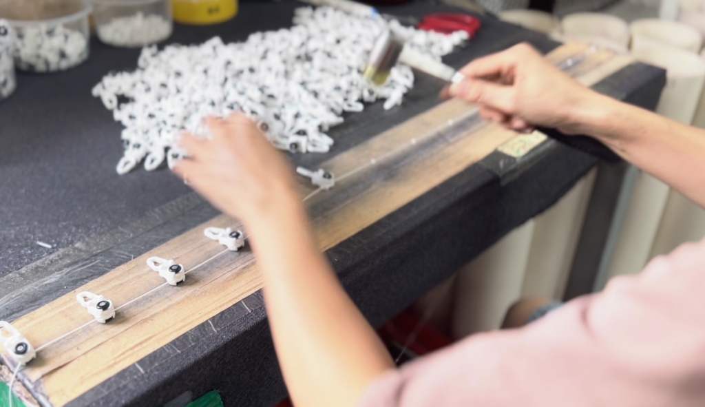 Factory worker manually tapping ball beads into aluminum curtain runner track during assembly process