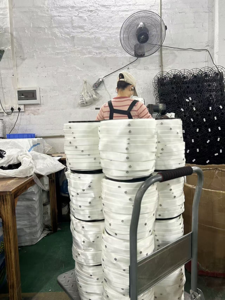 Female worker operating machine to press steel studs onto white curtain tape rolls at workstation
